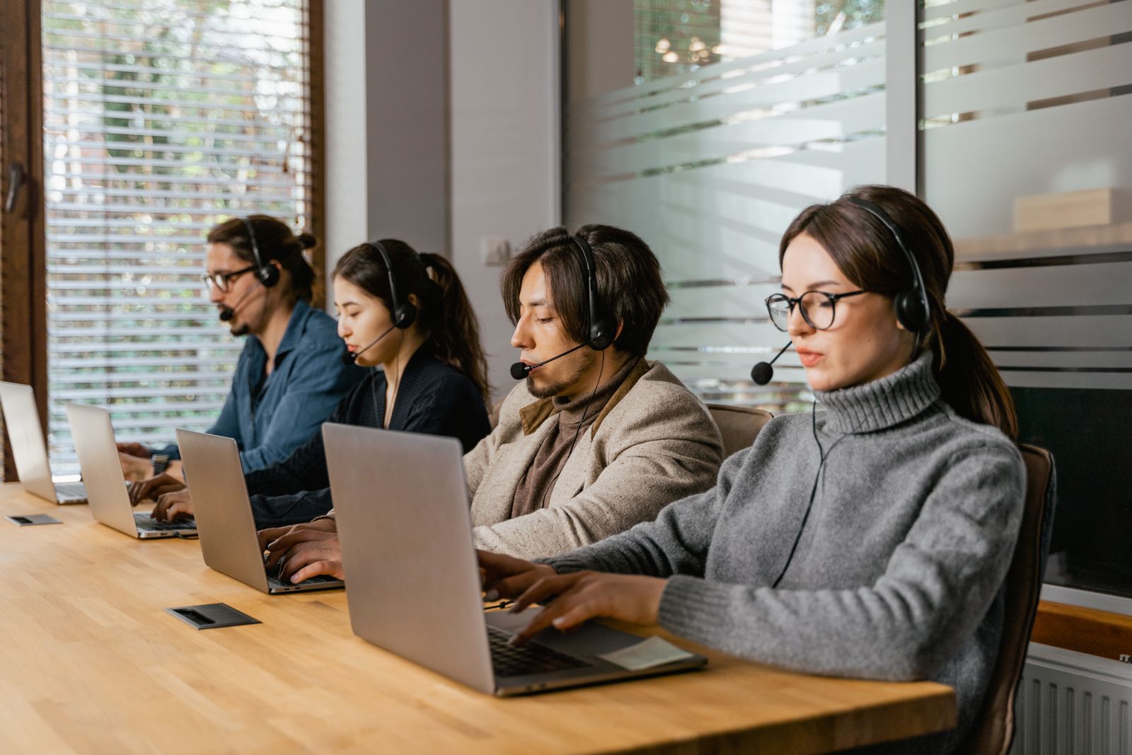 Team of support specialists wearing headsets working at laptops